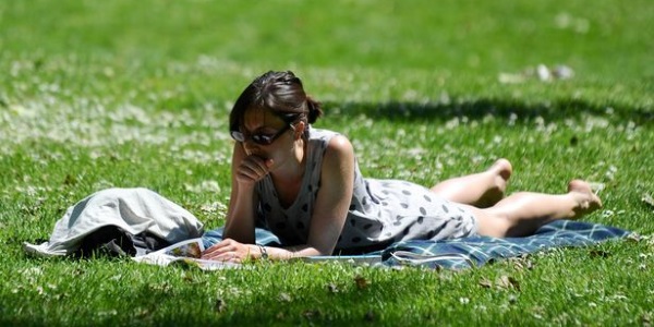 A woman reads a book in the sun as she sits in St James Park London